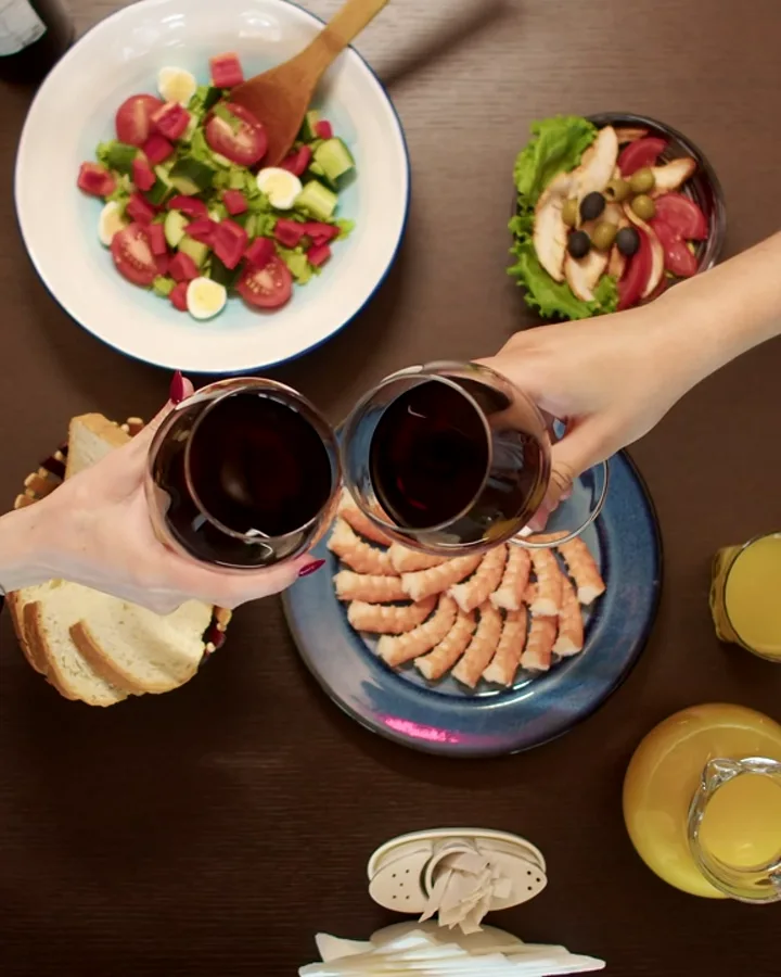 Gedeckter Tisch von oben, zwei Gläser Rotwein stoßen an